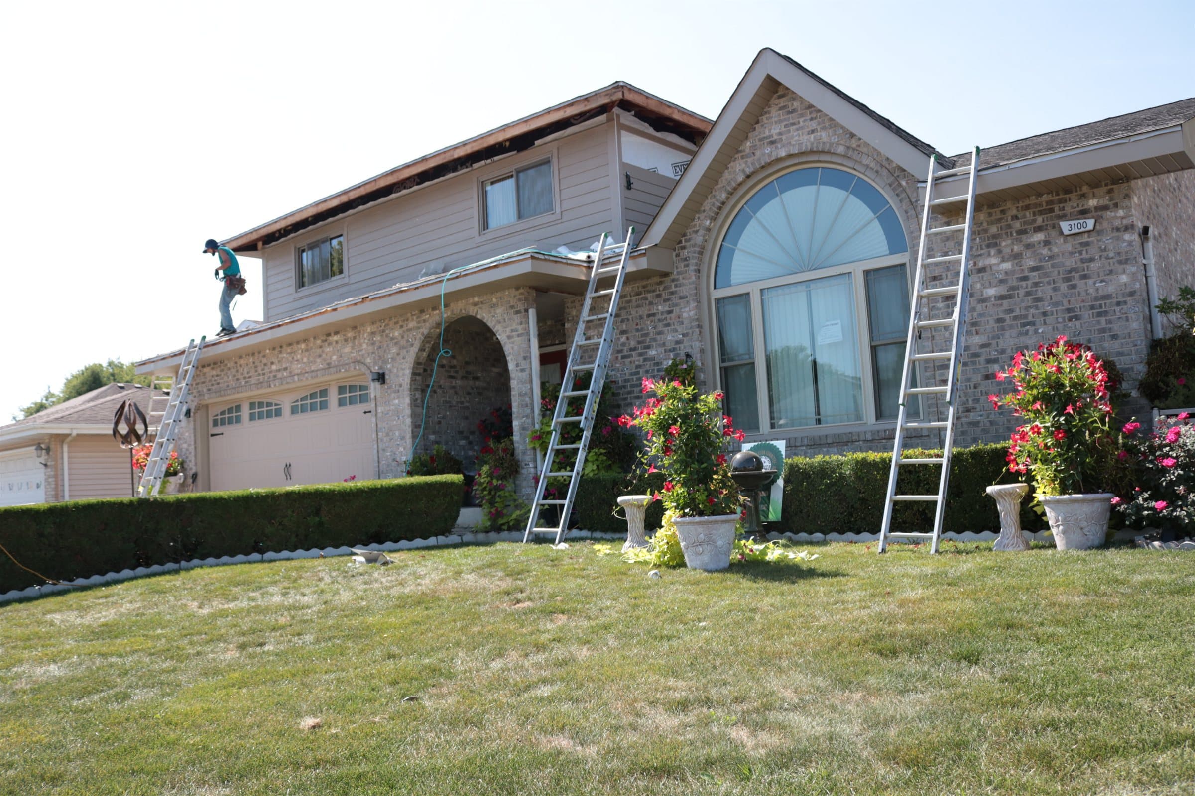 A house with a large arched front window during exterior work, ladders set against the elevation