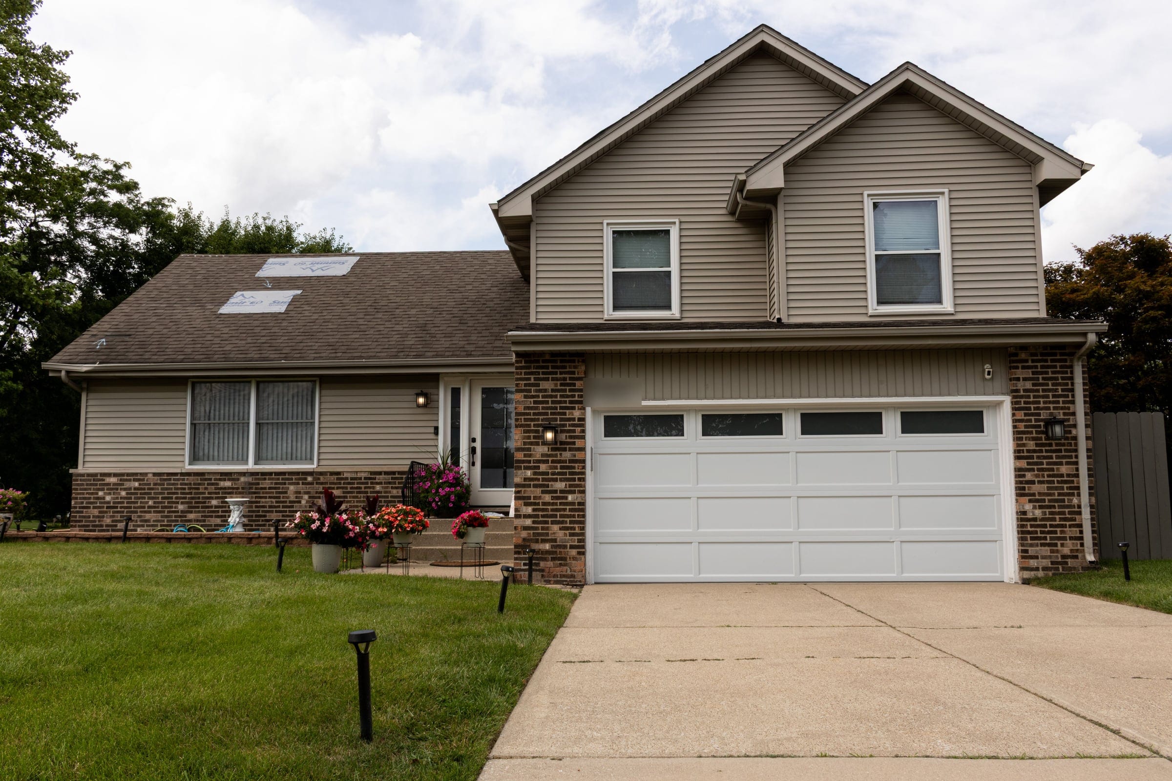A split-level home with a worn shingle roof and temporary patches over the damaged sections