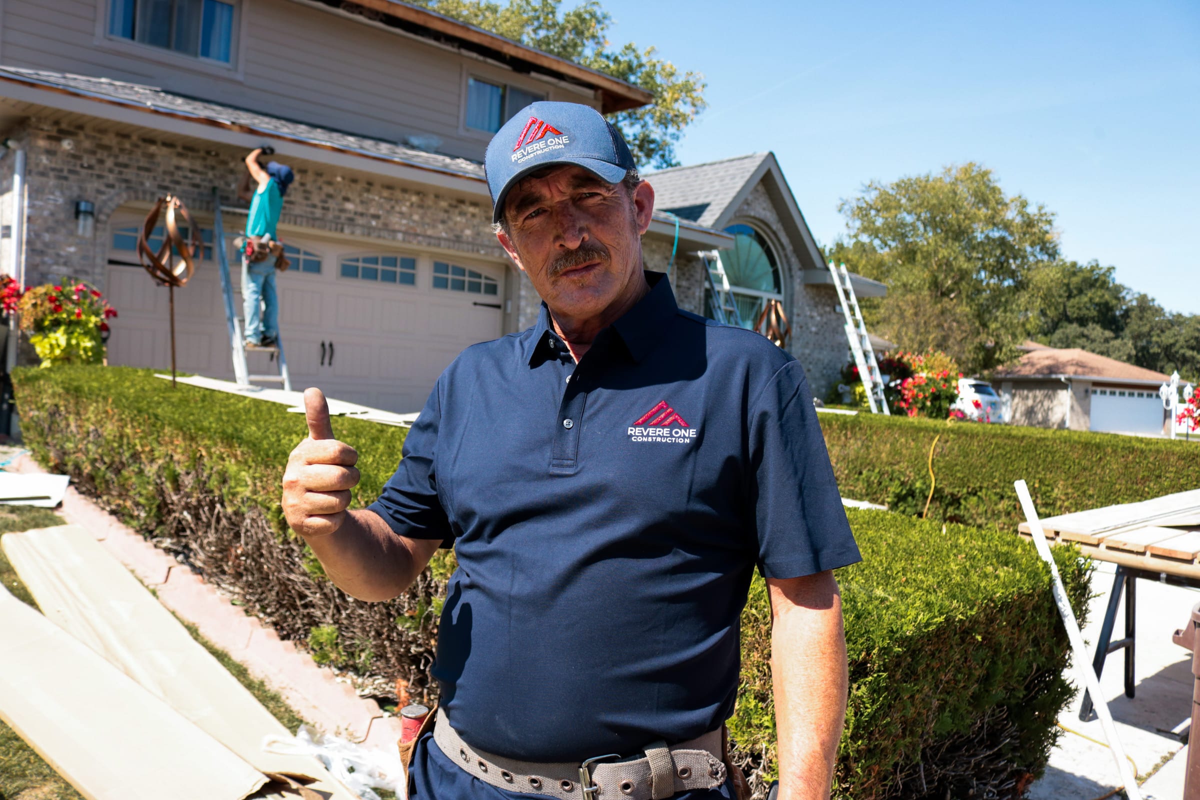 Francisco Jimenez of Revere One Construction on a residential job site, with a crew member working on the roof line behind him