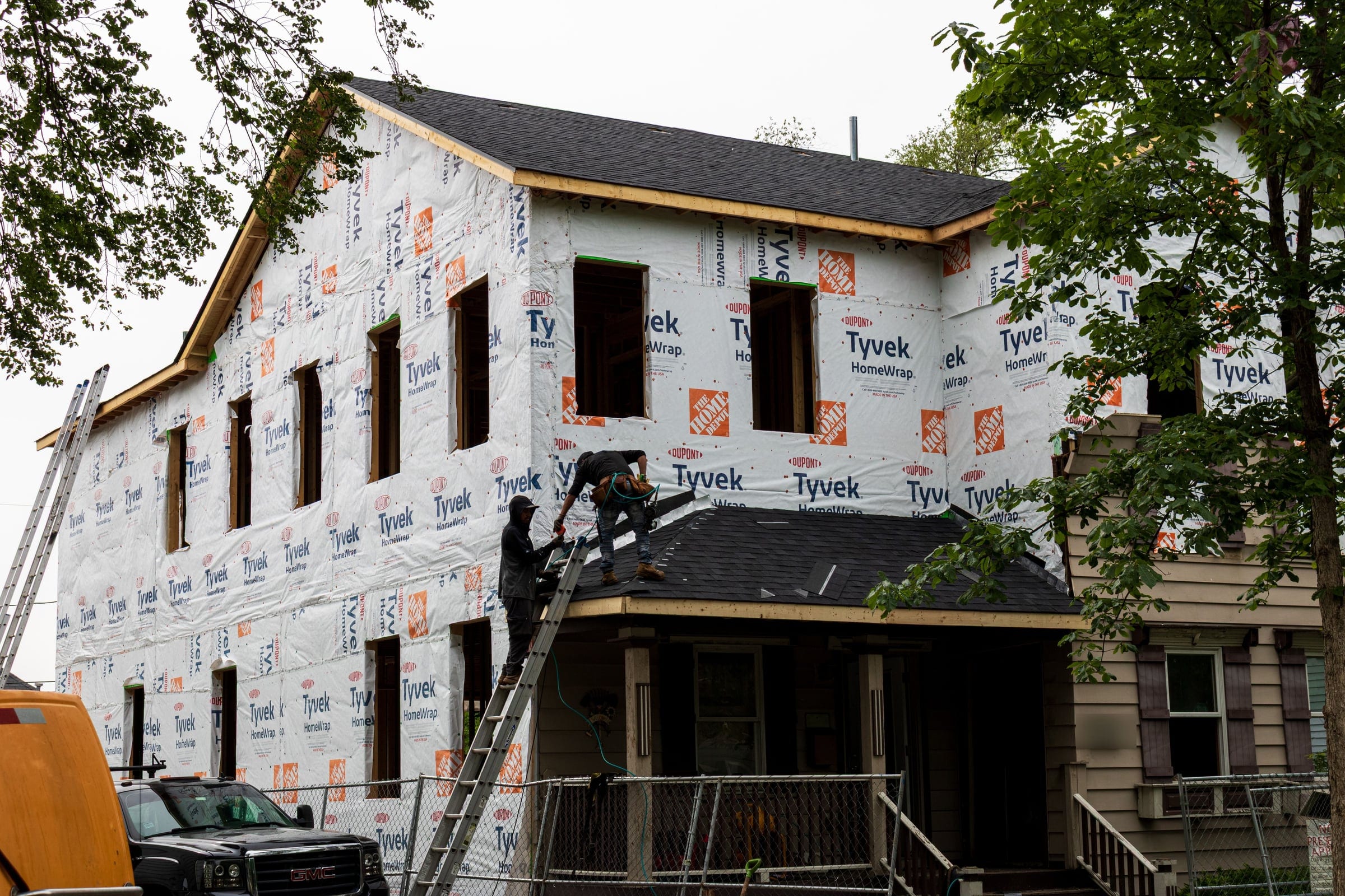 A house wrapped in house wrap during a full exterior remodel of roof, siding, fascia and windows, with roofers on the porch roof