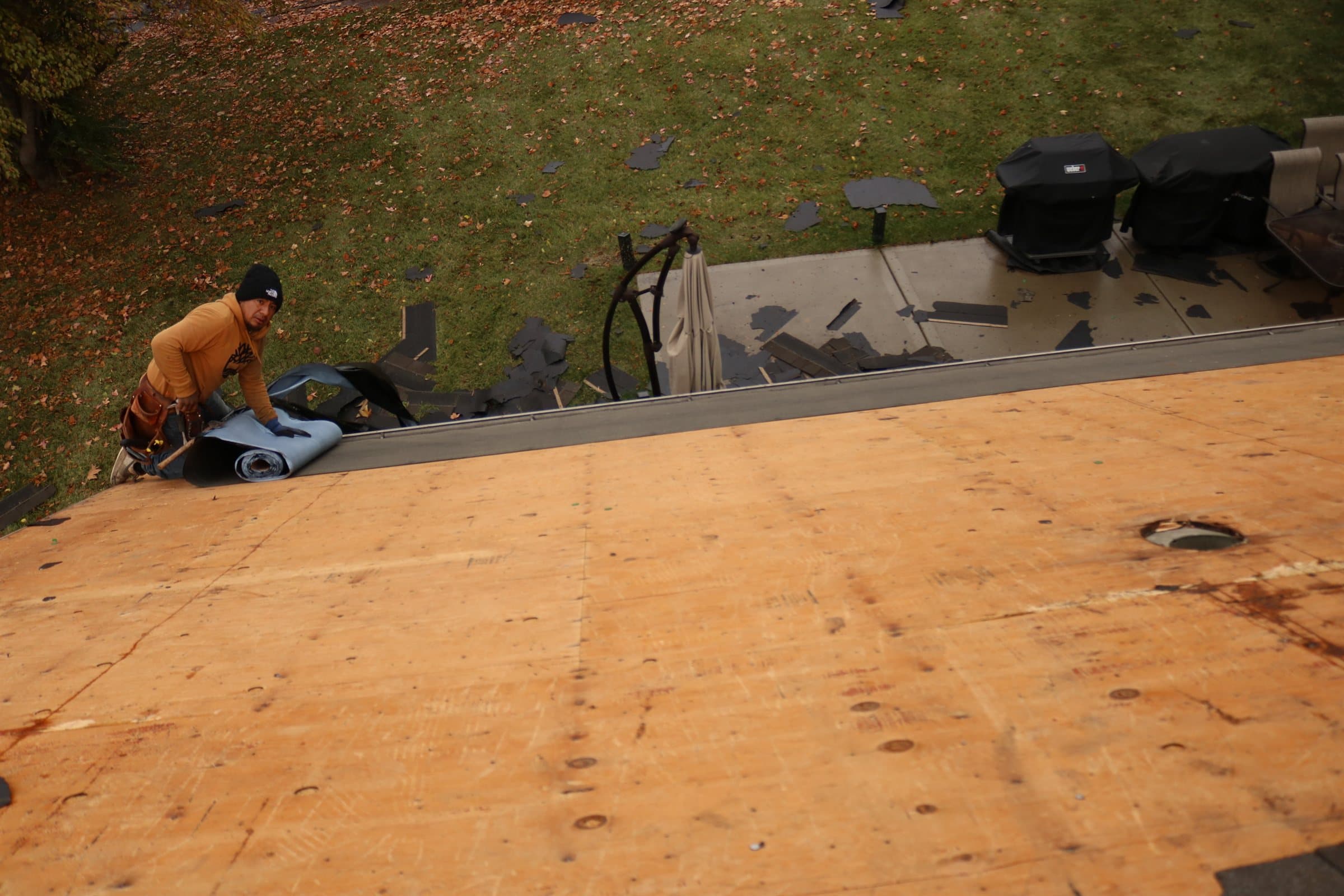 A bare plywood roof deck with a roofer unrolling material at the far edge