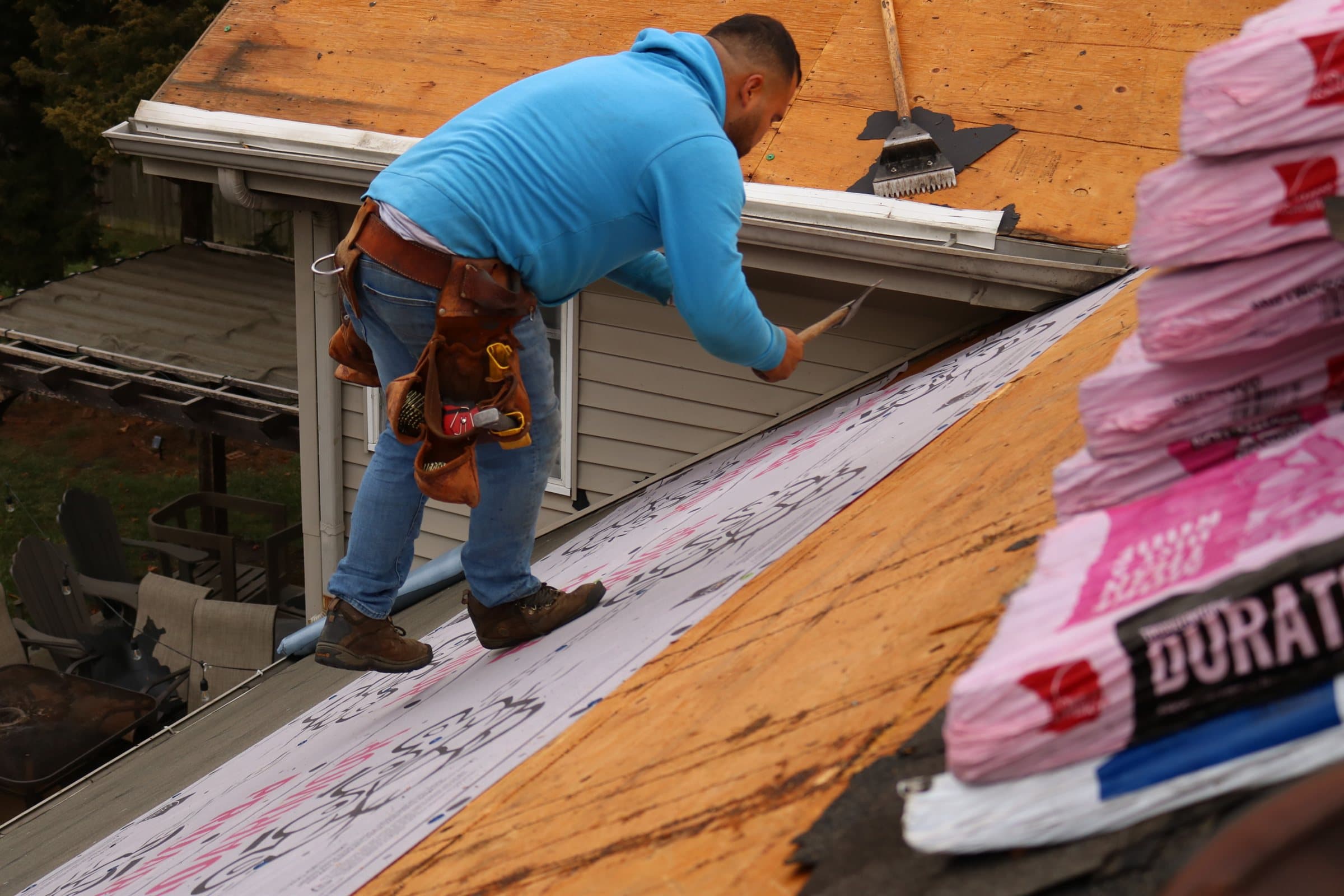 A roofer working at the eave with bundles of architectural shingles stacked beside him
