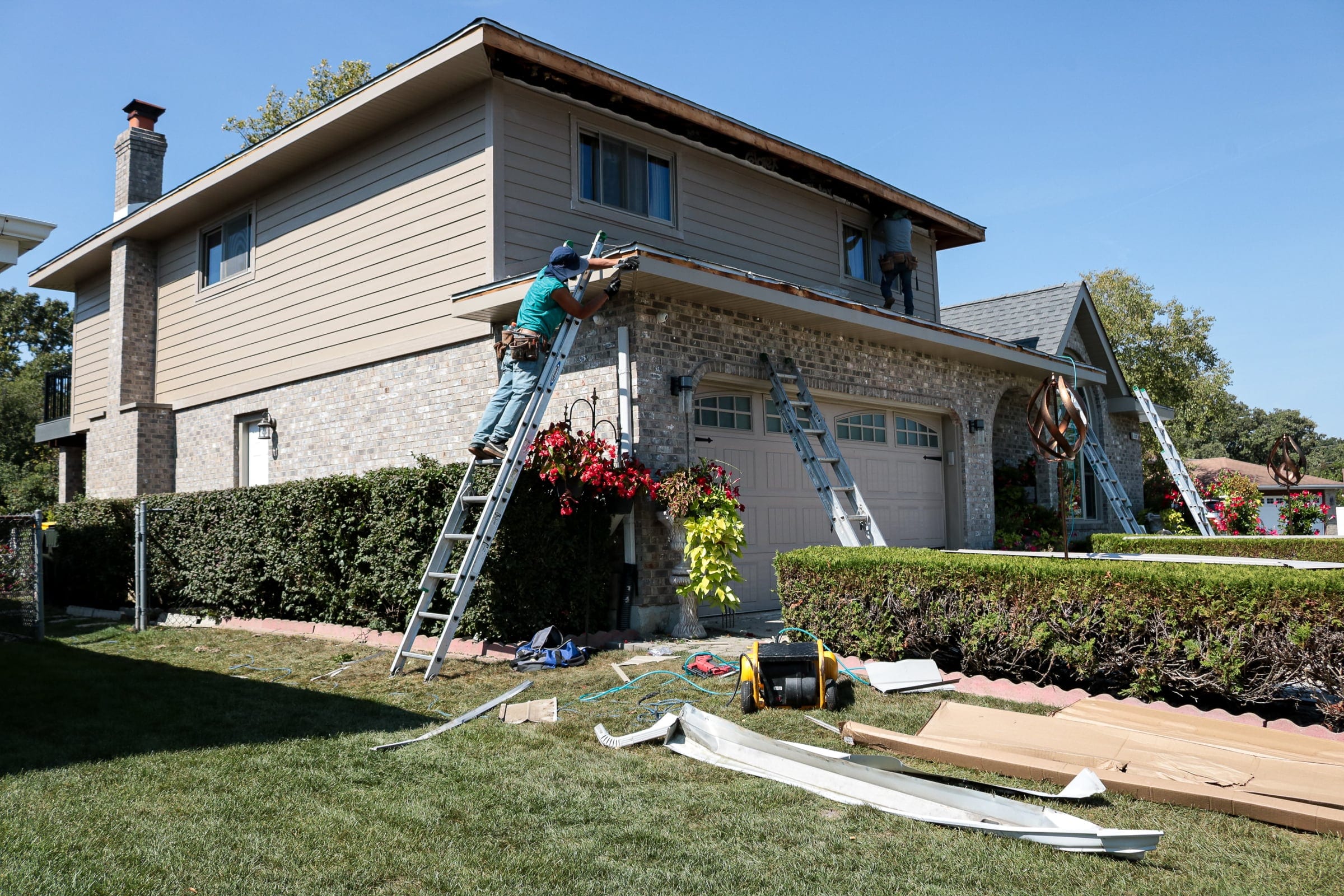 Crew on ladders working on the soffit and fascia of a two-storey brick and siding home